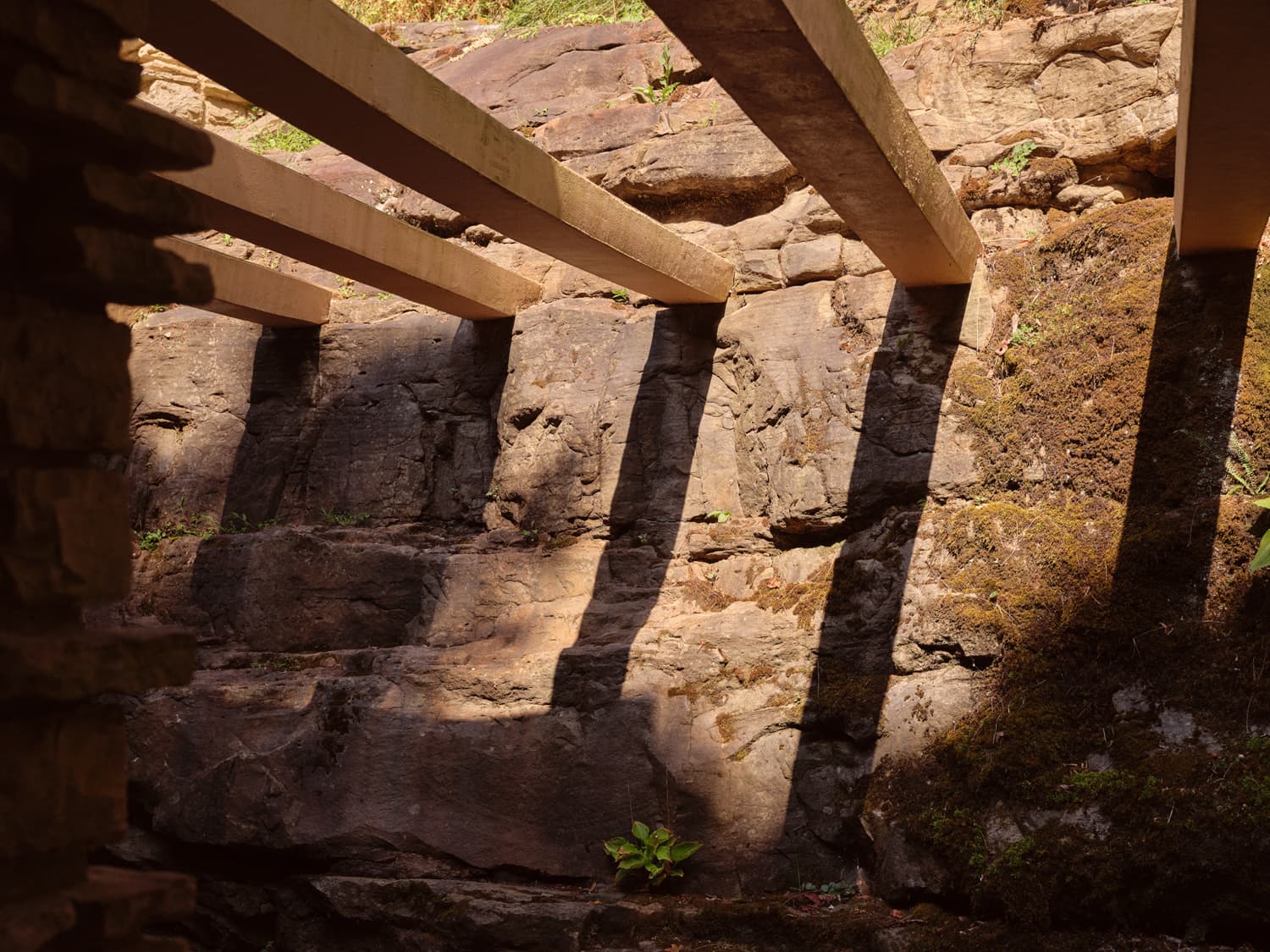 Sunlight casting shadows through concrete trellis beams onto natural rock ledge at Fallingwater