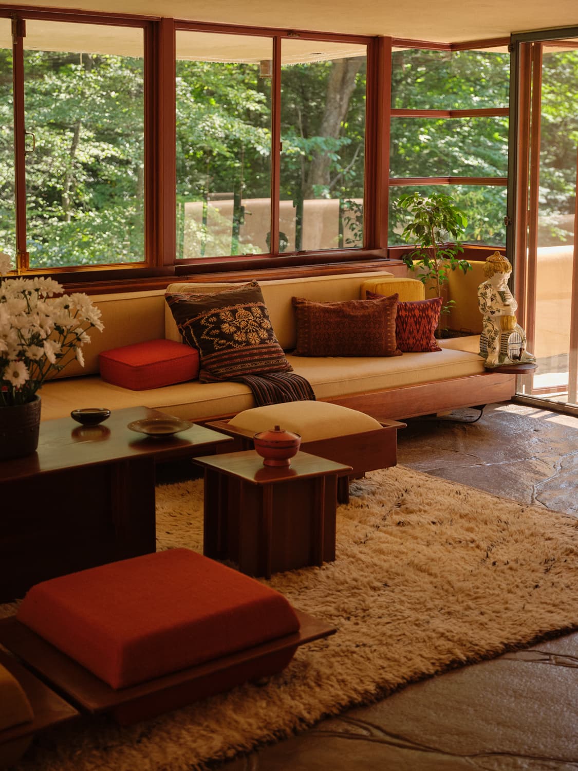 Corner of Fallingwater living room with built in sofa, patterned pillows, shag rug, and forest views