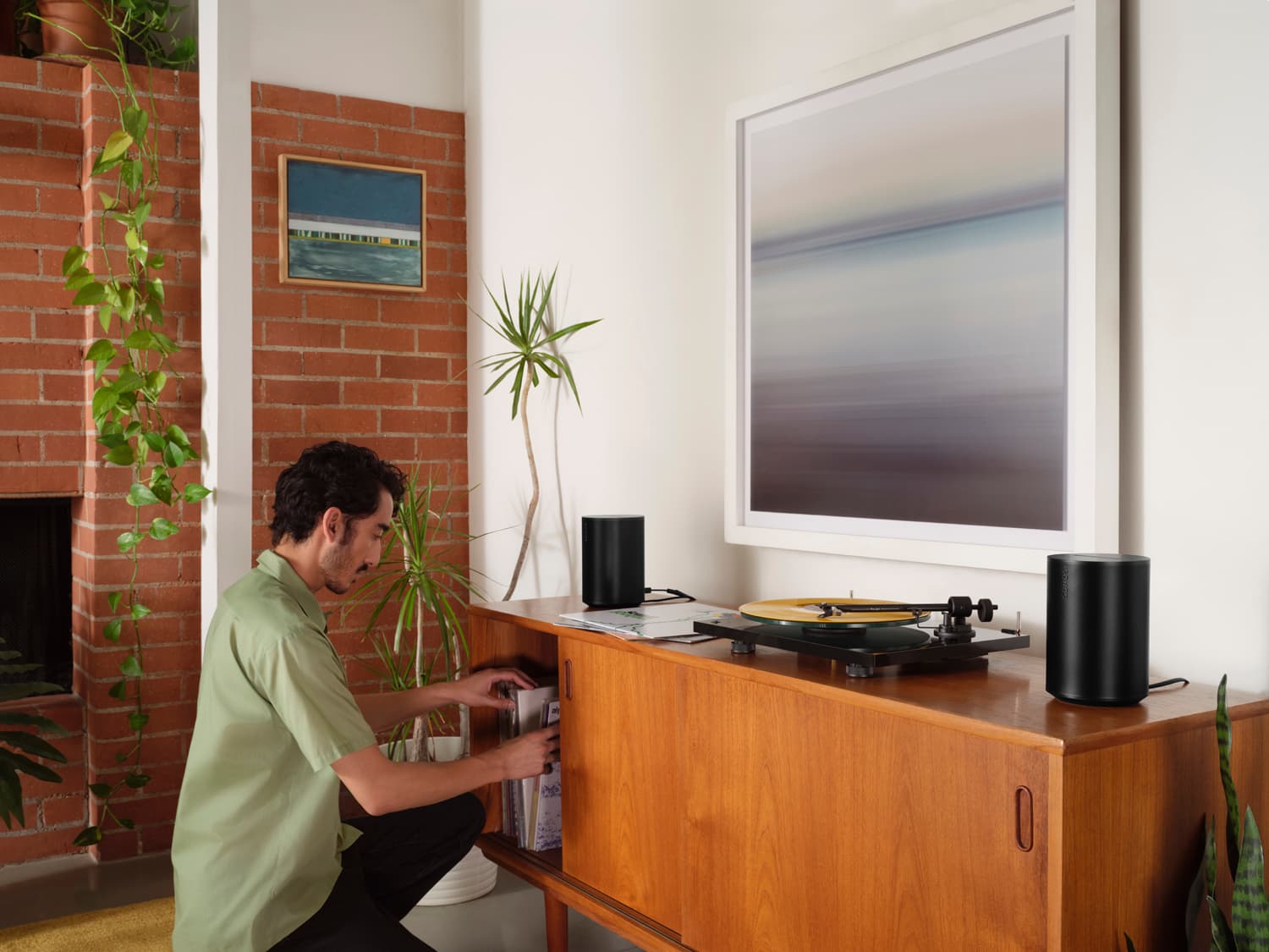 Man browsing vinyl records on a mid-century credenza with two black Sonos Era speakers and a turntable