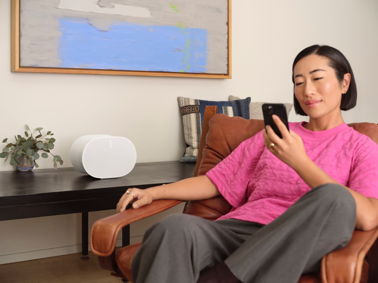 Woman on a leather chair checking her phone with a white Sonos Era 300 speaker on a side table