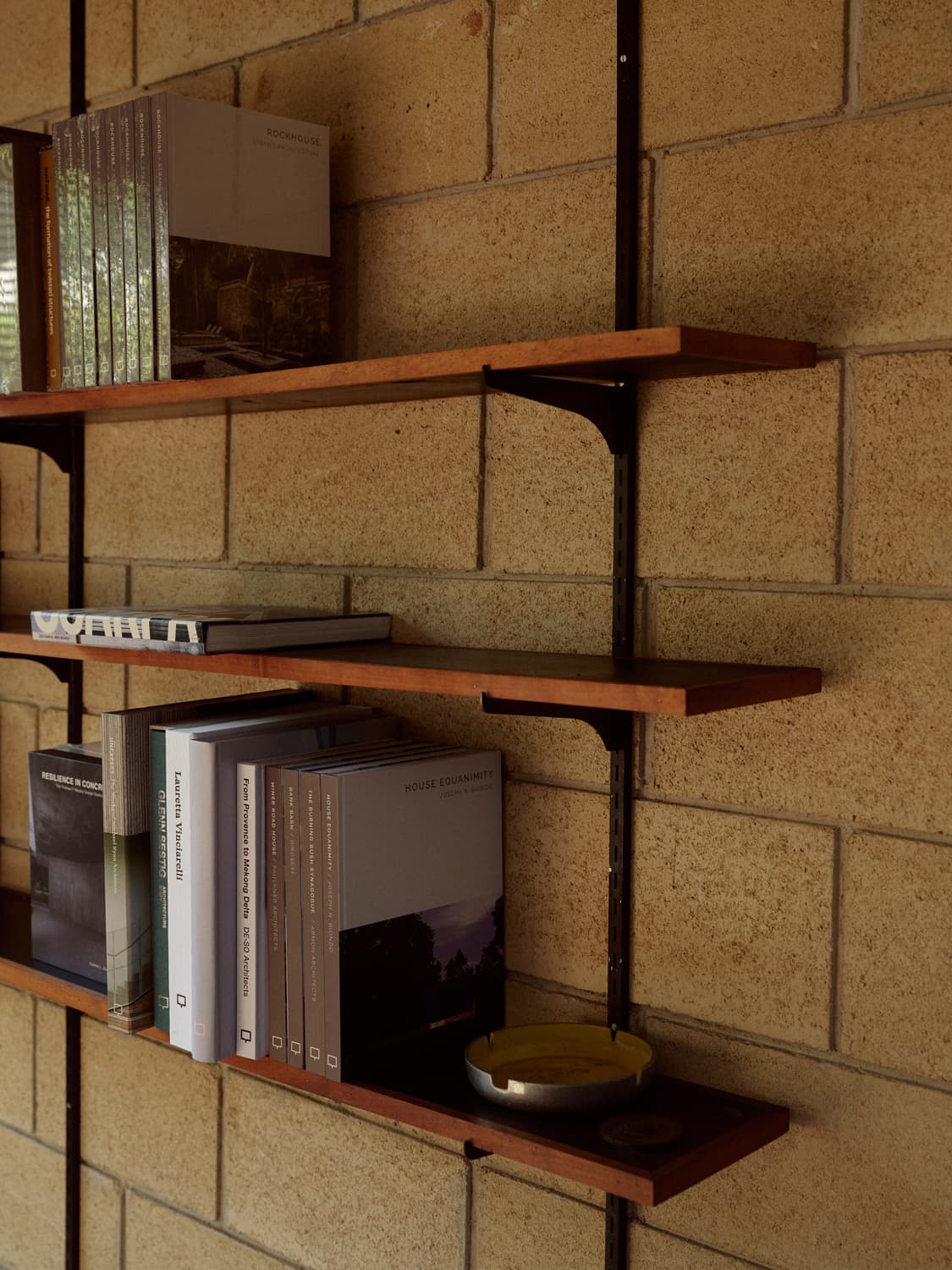 Wall mounted wood shelves with architecture books and an ashtray on a concrete block wall